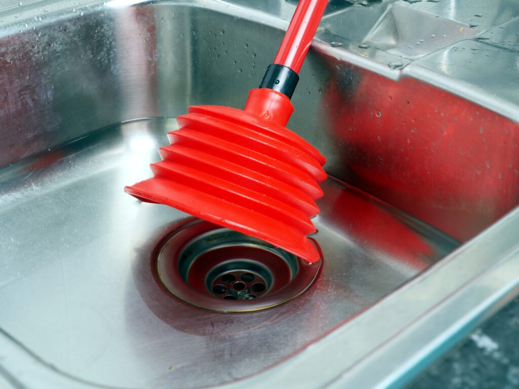 Un déboucheur à ventouse rouge utilisé sur un évier en inox pour éliminer un bouchon.