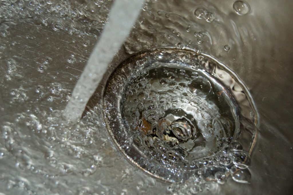 Gros plan sur l'eau s'écoulant librement dans le siphon d'un lavabo, indiquant un dégorgement réussi.