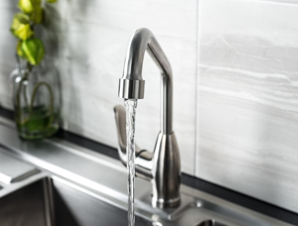 Eau claire s'écoulant d'un robinet en acier inoxydable dans une cuisine moderne avec un arrière-plan en marbre.