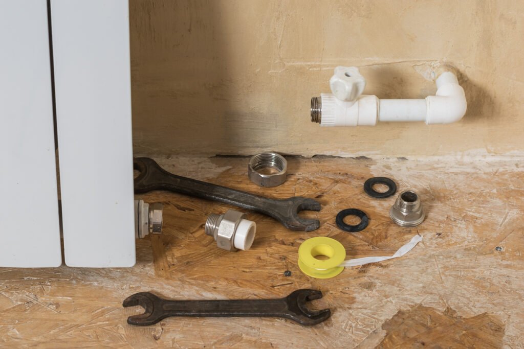 Outils et composants de plomberie disposés sur un sol en bois près d'un radiateur, prêts pour une réparation de fuite sur soudure.