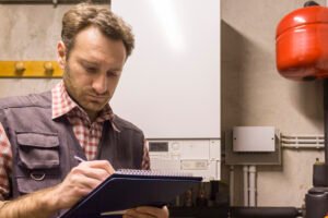 Technicien effectuant une révision de chaudière, prenant des notes devant une chaudière murale blanche.